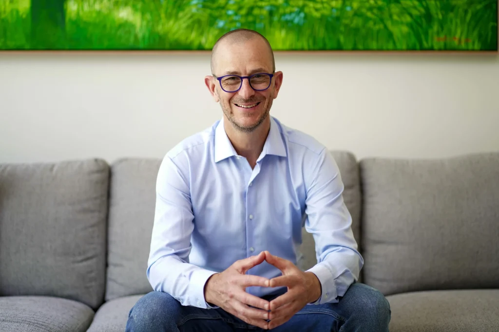Marc Wiesner, Certified Couples Master Coach, sitting on a grey sofa